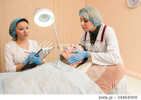 Two female doctors check male patient face in 38868906
