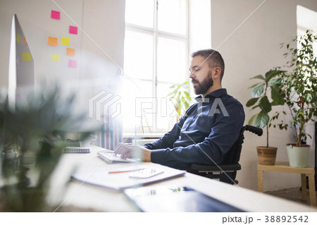 Businessman in wheelchair at the desk in his Businessman in wheelchair at the desk in his 38892542
