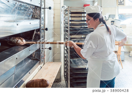 Baker woman getting bread out of bakery oven 38900428