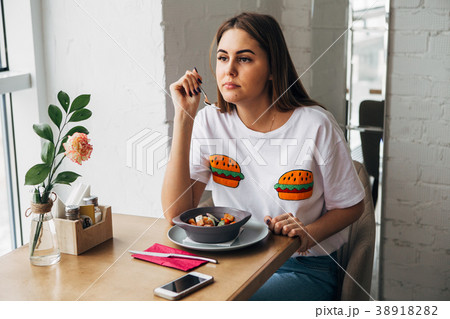 a beautiful young woman eats in a cafe and looks a beautiful young woman eats in a cafe and looks 38918282