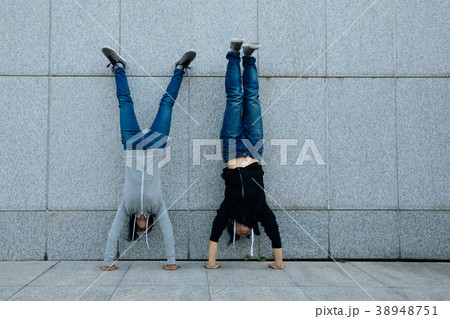 Two hipsters doing handstand against wall in city 38948751
