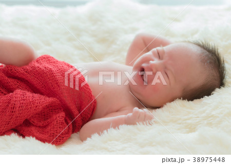 Portrait of crying baby girl lying in bed Portrait of crying baby girl lying in bed 38975448