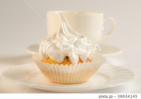 Cupcake with white icing on a plate and a cup of 39034145