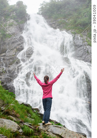 Girl standing with raised hands at waterfall. 39041009