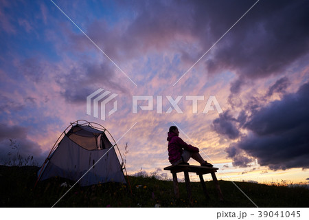 Young female tourist enjoying breathtaking sunset near tent in mountains in Romania 39041045