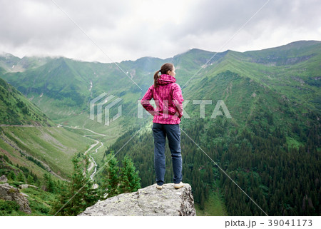Young female tourist standing on rock edge among magnificent green mountains with grassy slopes Young female tourist standing on rock edge among magnificent green mountains with grassy slopes 39041173