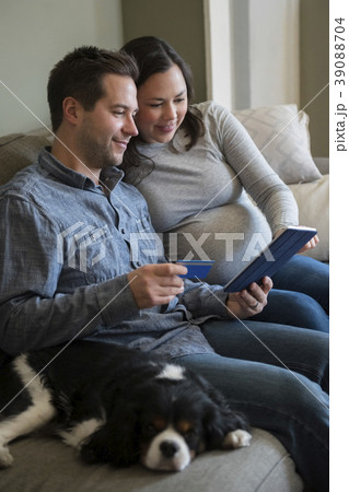 Mid adult couple shopping online in living room, sitting on sofa with puppy 39088704