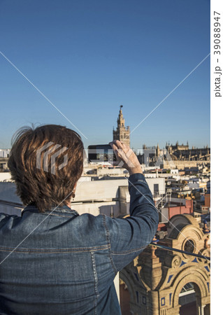 Spain, Andalusia, Seville, Plaza Nueva, Woman taking photo of cityscape and la Giralda with smartphone 39088947