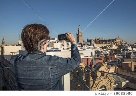 Spain, Andalusia, Seville, Plaza Nueva, Woman taking photo of cityscape and la Giralda with smartphone 39088990