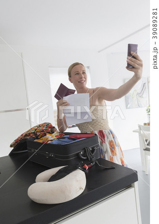 Happy mature woman packing suitcase for vacations and taking selfie 39089281