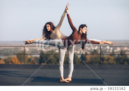 Two beautiful women doing yoga asana virabhadrasana on the roof 39152162