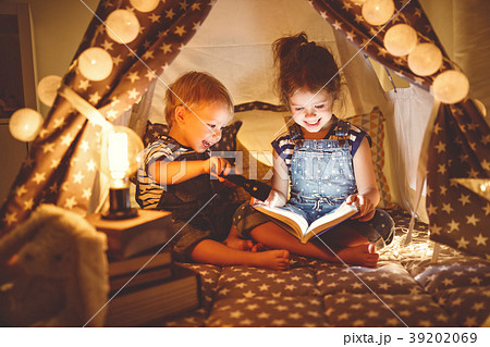 children boy and girl reading book with flashlight in tent children boy and girl reading book with flashlight in tent 39202069