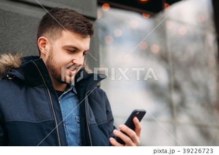 Handsome man in a jacket uses a phone standing on 39226723