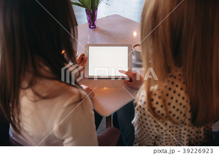 Two girls use a tablet while sitting in a cafe and 39226923