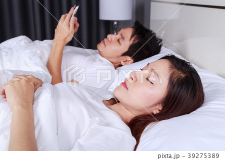 woman in bed with her sleeping and her husband texting on smartp woman in bed with her sleeping and her husband texting on smartp 39275389