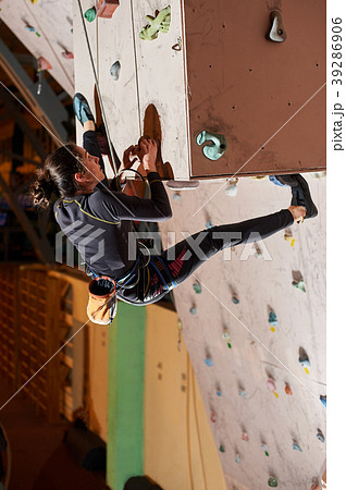 Young woman climbing up on practice wall in gym Young woman climbing up on practice wall in gym 39286906