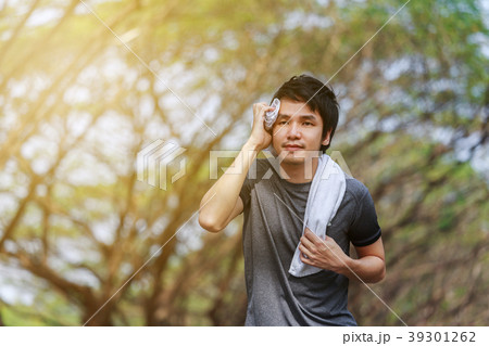 sporty man running and wiping his sweat with a towel in the park sporty man running and wiping his sweat with a towel in the park 39301262