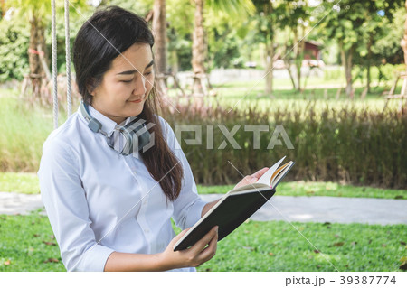 smiling young woman reading the book and sitting on the grass in 39387774