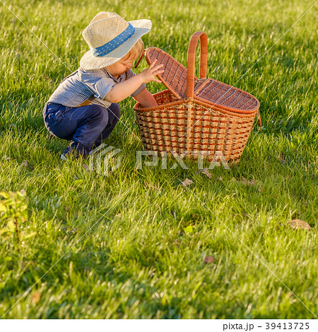 Toddler child outdoors. One year old baby boy wearing straw hat looking in picnic basket Toddler child outdoors. One year old baby boy wearing straw hat looking in picnic basket 39413725