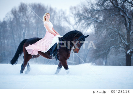Young woman in dress riding horse on winter field 39428118