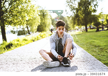 Runner in the city sitting on concrete path tying 39431674