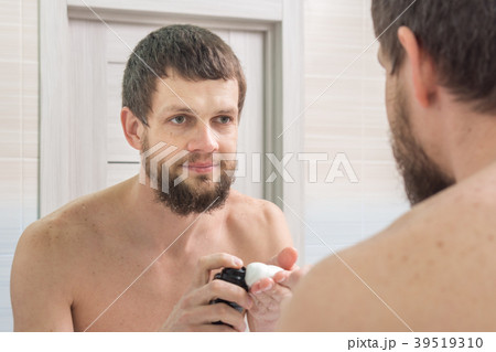An unshaven man applies a shaving foam on  39519310