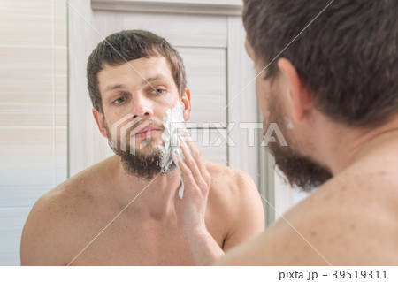 A man is applying shaving foam to his face preparing to shave 39519311
