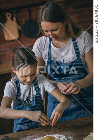 Girl and mother cracking eggs to flour 39564901