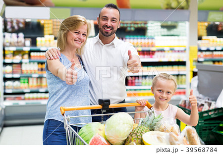 Happy family standing with full cart in supermarket Happy family standing with full cart in supermarket 39568784