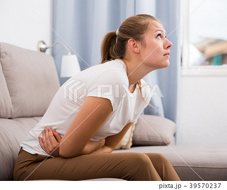 Girl is sitting unhappy because she has a stomach ache Girl is sitting unhappy because she has a stomach ache 39570237