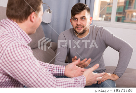 Happy male enjoying сonversation with friend on sofa 39571236