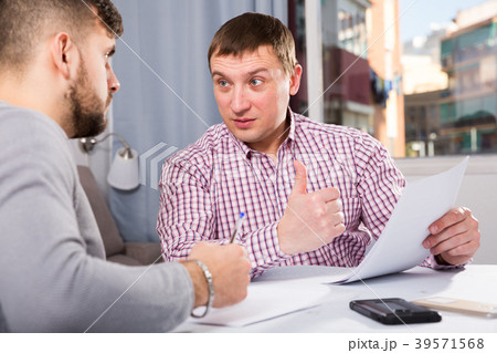 Cheerful man reading documents with friend at home table 39571568