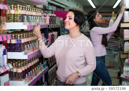 woman picking scented spray from shelf in cosmetics store 39572196