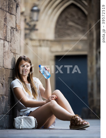 Woman sitting near old stone wall drinking water 39572519