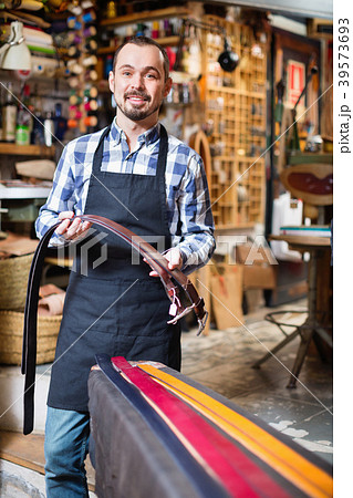 Smiling male worker showing new belts in leather workshop 39573693