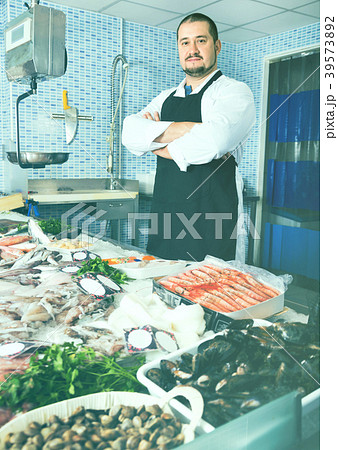 Seller in black apron showing fish on his counter Seller in black apron showing fish on his counter 39573892