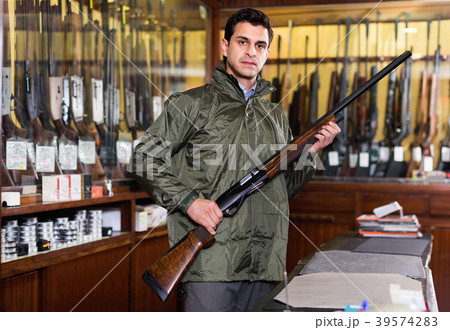 Hunter male wearing windbreaker in hunting shop with rifle in hands Hunter male wearing windbreaker in hunting shop with rifle in hands 39574283