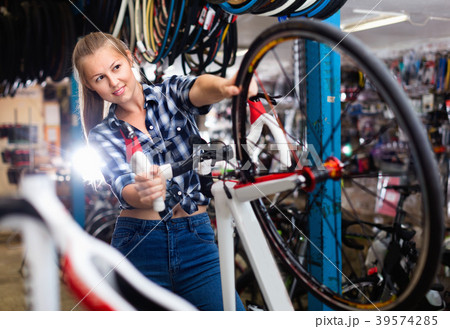 Young female is cheking wheels of bicycle in workshop. 39574285