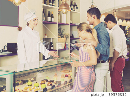 Cheerful pastry chef female is offering cakes from showcase Cheerful pastry chef female is offering cakes from showcase 39576352