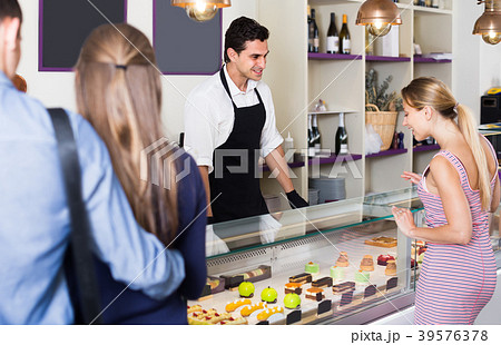 Young seller helping clients to choose sweets 39576378