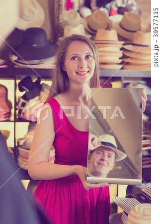 assistant holding mirror and showing man his reflection in hats store 39577115