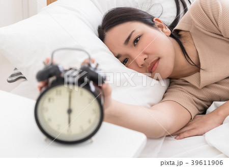 Asian woman on bed reaching out to stop the alarm Asian woman on bed reaching out to stop the alarm 39611906