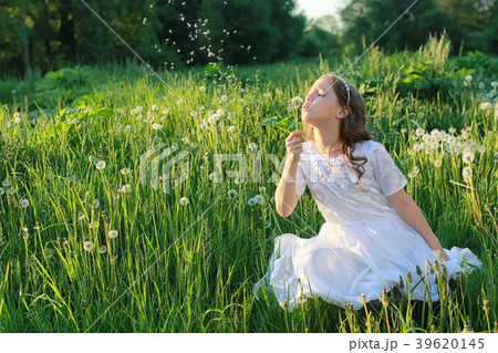 Teen blowing seeds from a dandelion flower in a Teen blowing seeds from a dandelion flower in a 39620145