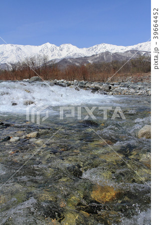 白馬山麓の春 雪解けの川と北アルプスの写真素材
