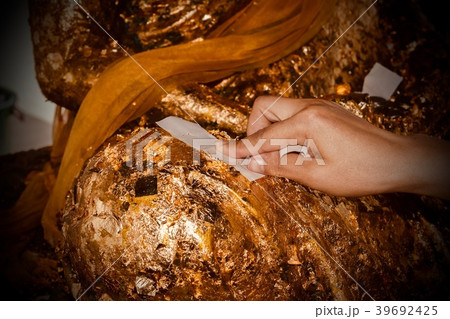 People stick gold plate on the Buddha statue. 39692425