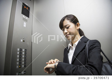 エレベーターの中で時計をみるビジネスウーマンの写真素材