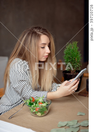 Young woman sitting at the table looks at phone 39710716