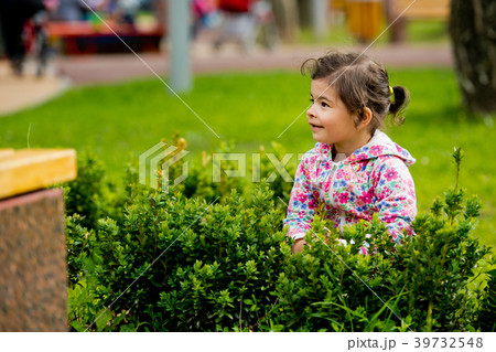 Little cute girl sitting in green bush. 39732548