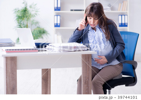 Pregnant woman struggling to do work in office Pregnant woman struggling to do work in office 39744101