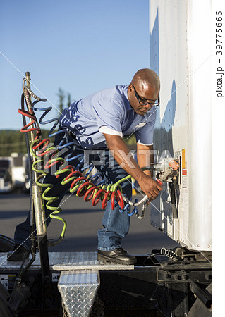 Black man truck driver attaching power cables from truck tractor to trailer at a truck stop. Black man truck driver attaching power cables from truck tractor to trailer at a truck stop. 39775666